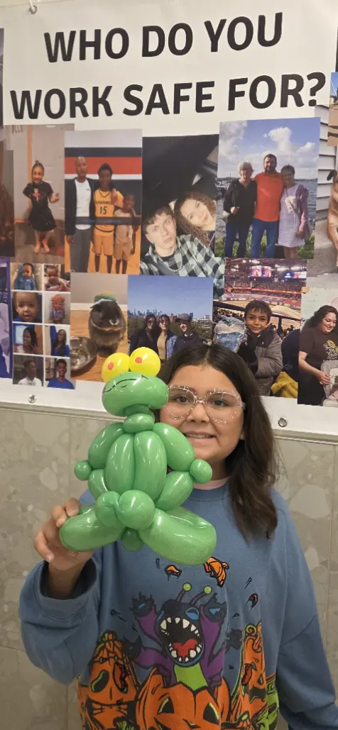 NLX Beverage Solutions employee holding a green balloon frog beside a Safety Week display in New Lenox